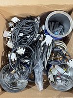 Top view of box showing tangled black cables with multiple white DVI connectors and two metal cans