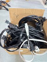 Box containing tangle of multiple black power cords showing assorted plug types