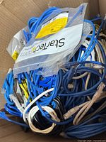 Open box filled with blue, white, yellow and black Cat5 Ethernet cables, RJ45 ends visible, some sealed StarTech.com package