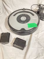 Roomba robot vacuum with dock and two loose accessories on white background