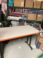 Full view of desk showing white top, orange edge, black metal T-legs