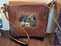 Front of brown leather shoulder bag showing tooled decoration, Las Meninas image panel, flap, strap and hardware