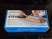 Box top showing Sharp Pebble dual-grit sharpening stone on bamboo base