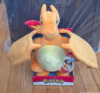 Front view of Charizard plush seated in cardboard Pokémon display base, swing tag visible