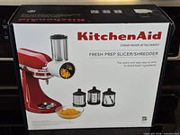 Front of sealed KitchenAid Fresh Prep Slicer/Shredder box showing attachment image and three blades