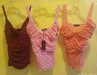 Front view of three sleeveless layered tops in red, pink and peach on hangers