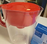 Side view of red-top Brita pitcher next to filter box