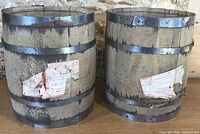 Front view of both wooden barrels with metal bands and torn CN labels