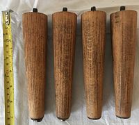 Four wooden tapered legs side by side with tape measure showing length