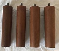 Four teak cylindrical legs upright showing threaded bolts