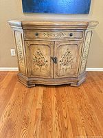 Front view of cabinet showing drawer, doors, floral painting, carved details