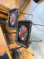 Two black floral metal TV trays on black folding stands