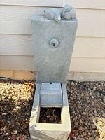 Full view of grey rectangular fountain with birds on top, front spout and basin