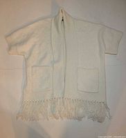 Front view of cream knit sweater showing open front, pockets, fringe hem