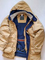 Front view of tan Boat House Row hooded parka open to show navy quilted lining and pockets