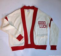 Front view of cream cardigan with red trim and GOOD LUCK text