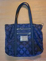 Front view of Coach Poppy tote showing signature C canvas, leather trim, front zip pocket and metal plaque