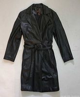 Front view of black leather trench coat laid flat showing belt and lapel