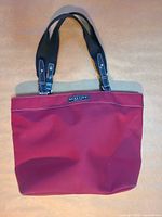 Front view of burgundy Kenneth Cole Reaction tote bag showing logo, handles, stitching