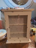 Front view of white wooden key cabinet with glass door and bee motif