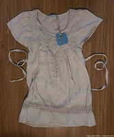 Front view of beige linen dress with lace detail and waist ties