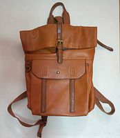 Front view of brown faux leather backpack showing fold-over top, front pocket, hardware