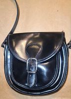 Front view of black patent leather shoulder bag with flap and buckle