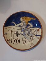 Front view of hand-painted plate showing winged figure and sheep design