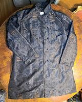 Front view of black brocade jacket laid flat showing frog toggles and pattern