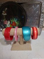 Four moonglow lucite bangles on display stand, colours red, pink, teal