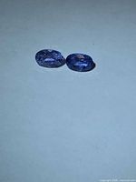 Two oval faceted blue sapphires on neutral background