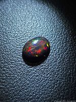 Front view of oval black opal with multicolored play-of-color