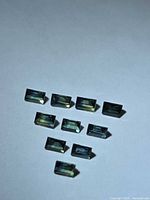 Ten rectangular green-blue sapphires on flat surface