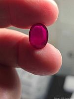 Front view of loose oval ruby held between fingers