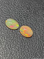 Two oval cabochon opals on black textured background showing colour play