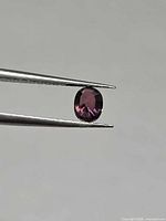 Oval purplish-pink sapphire held in tweezers, side profile