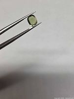 Side profile of green sapphire held by tweezers