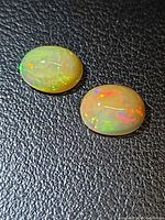 two oval opal cabochons on textured black background showing multicolour fire