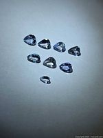 Eight pear-cut bluish-violet gemstones on neutral background