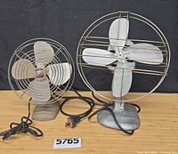 Front view of both metal fans showing blades, cages, bases, and power cords