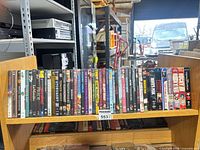 Two wooden shelves filled with DVD cases along the top row and VHS tapes partially visible on the lower shelf