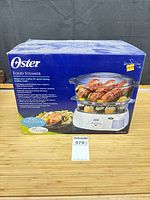 Front of boxed Oster food steamer showing product image and branding