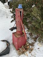 Front view of red wooden hand pump with cast iron spout and detached handle on box base in snow