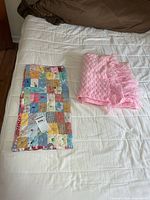 Both textile items on bed: folded pink crocheted blanket and laid-out patchwork baby quilt