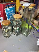 Three glass canisters side by side showing relative sizes and lids; two contain buttons