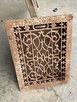 Front view of ornate cast iron floor grate showing scroll design and rust patina