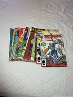 Stack of approximately 18 vintage comic books on bed, mix of titles visible