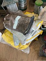 Stack showing brown gloves on top of grey gloves and packaged yellow raincoat