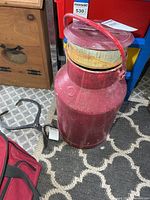 Full view of red painted metal milk can with lid and handle