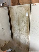 Front view of beige metal two-door cabinet showing rust spots and handle